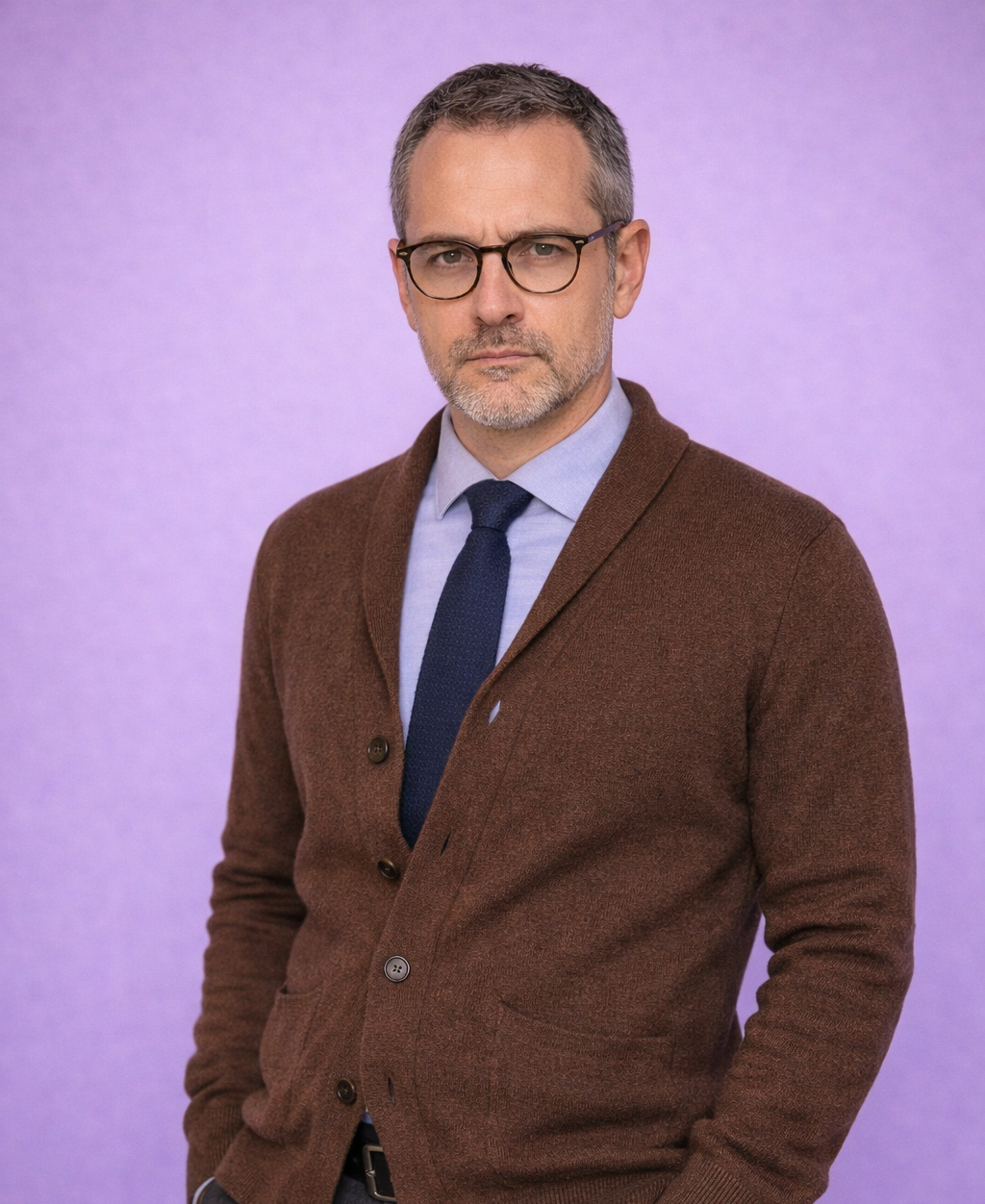 A middle aged man, nerdy looking, tie, cardigan and button down shirt. He has glasses.
